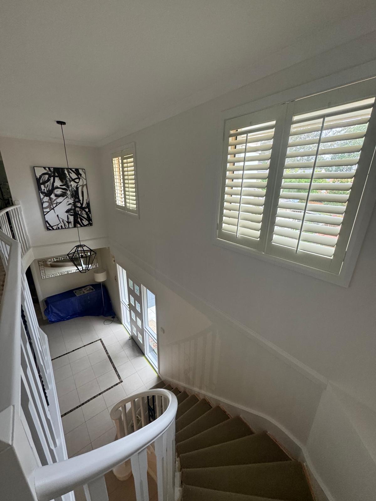 Freshly painted white stairwell with plantation shutters and a pendant light